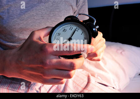 a young caucasian man wearing pajamas in bed setting the alarm clock at 7 before lie down Stock Photo