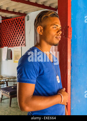 A twenty something Afro-Cuban man stands in a very colorful red doorway with a blue wall that matches the color of his shirt. Stock Photo