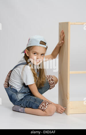 Little girl - collector of furniture twists the screw on the wooden frame of the chest Stock Photo