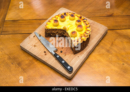 Traditional Easter simnel cake with marzipan topping and balls cut with portion removed on a wooden chopping board with a large, sharp kitchen knife Stock Photo