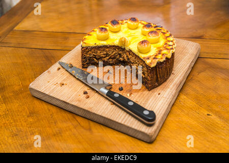 Traditional Easter simnel cake with marzipan topping and balls cut with portion removed on a wooden chopping board with a large, sharp kitchen knife Stock Photo