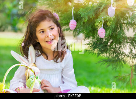 Portrait of nice little girl playing traditional Easter game, happy egg hunting, having fun at spring park in religious holiday Stock Photo