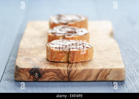 baguette slices with chocolate hazelnut spread on olive board Stock Photo