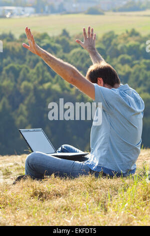 young man using laptop sitting on the grass on the hillside Stock Photo