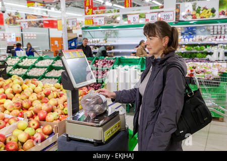 Young woman weighing potatoes on electronic scales in produce department of the Magnit store. Stock Photo