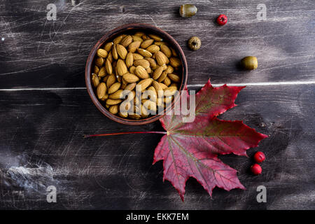 Fall background: raw almonds in bowl and red maple leaf on rustic wooden table, top view. Stock Photo