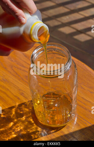 Close up of someone pouring thick, golden, raw honey from a plastic jug into a glass jar Stock Photo