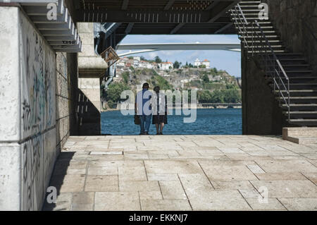 An old couple walk hand in hand under the iron brigde of Oporto, Portugal Stock Photo