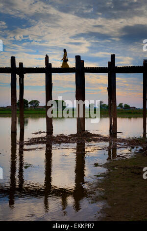 A single isolated figure, a woman in a long dress, strides across, U Bein's Bridge, itself silhouetted, and reflected. Stock Photo