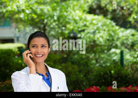 Closeup portrait, friendly, young smiling confident female doctor, healthcare professional talking on phone outside Stock Photo