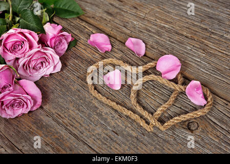 Rope hearts on rustic wood with pink rose and loose petals. Stock Photo