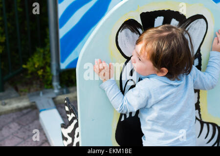 A 2 year old boy hugging a painting of a zebra at a zoo. Stock Photo