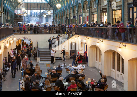 Crowds of tourists and shoppers listen to live music from a group of buskers in the South Hall of Covent Garden, London Stock Photo