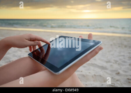 Woman holding a tablet on the beach during warm sunset Stock Photo