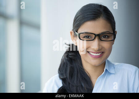 Closeup portrait, young professional, beautiful confident adult woman in blue shirt, with black glasses, smiling isolated indoor Stock Photo