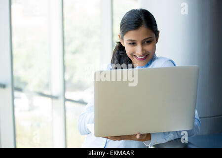 Closeup portrait, young, attractive wife, mother, standing, smiling looking, surfing the silver laptop. Isolated glass window in Stock Photo