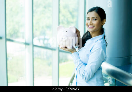 Closeup portrait happy, smiling business woman, holding pink piggy bank, isolated indoors office background. Financial budget sa Stock Photo