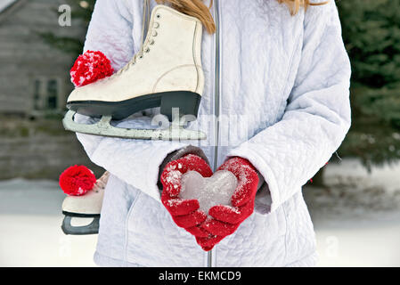 Young teenage girl with ice skates holding an ice heart in red gloves. Stock Photo