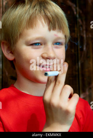 Portrait of Child blond boy smoking cigarette with dark wooden background behind him Stock Photo