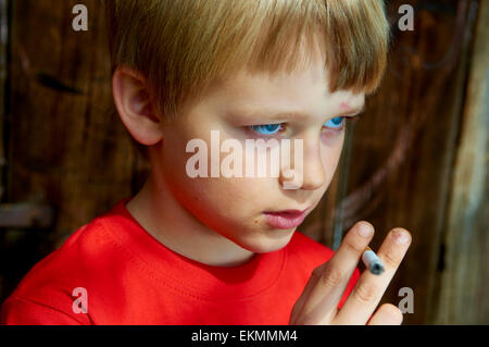 Portrait of Child blond boy smoking cigarette with dark wooden background behind him Stock Photo