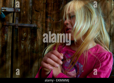 Close up of face of crying child blond girl with wooden wall background outside Stock Photo