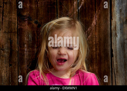 Close up of face of crying child blond girl with wooden wall background outside Stock Photo