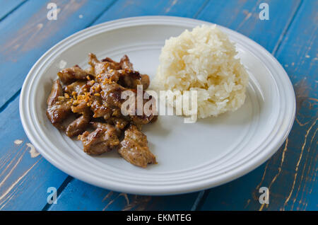 Garlic and pepper fried pork with sticky rice on plate against blue wooden background Stock Photo