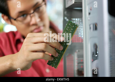 Young asian shop owner working in computer store, repairing computer and adding ram to pc. Focus on hand holding bank of RAM Stock Photo