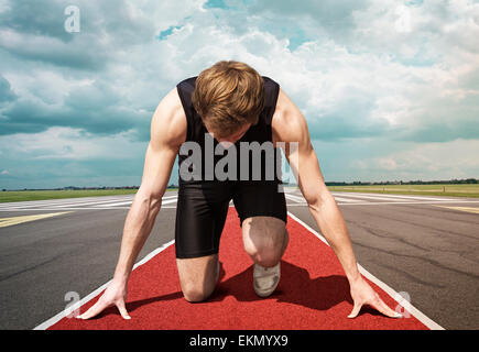 Male version of airport runway starter. Runner in start position kneels with lowered head on a red tartan surface. Stock Photo