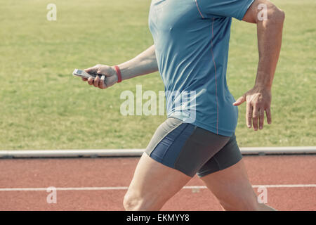 Runner in a stadium checks his fitness results on a smart phone while running. Stock Photo