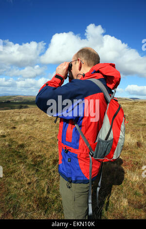 Man looking through binoculars in the countryside whilst out hill walking Stock Photo