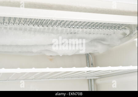time to defrost an ice laden inefficient deep freezer with built up layers of ice  frozen water on the elements and shelf inside Stock Photo