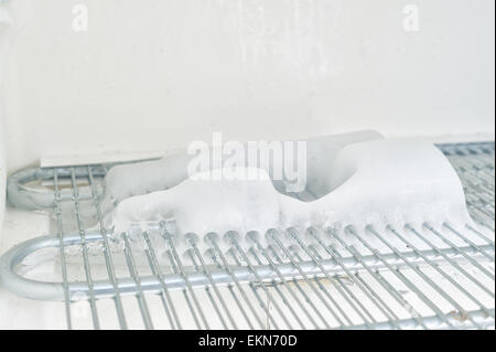 time to defrost an ice laden inefficient deep freezer with built up layers of ice  frozen water on the elements and shelf inside Stock Photo