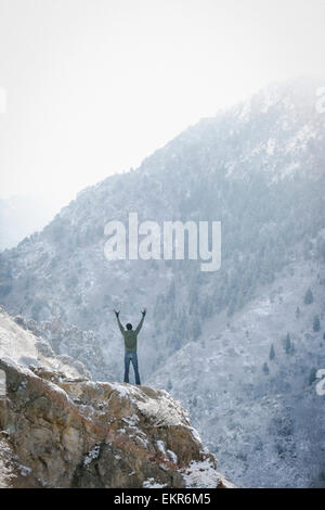 A man greeting the sun, with his arms raised on a rock outcrop in the mountains. Stock Photo