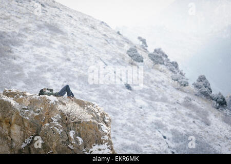 A man, a hiker in the mountains, taking a rest lying on a rock outcrop above a valley. Stock Photo