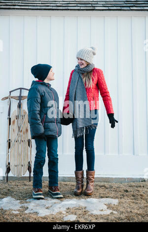Two children, brother and sister, standing side by side in winter coats in a yard. Stock Photo