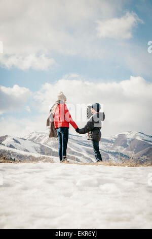 A brother and sister holding hands and looking at the snowy landscape. Stock Photo