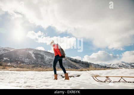 A young girl in a red jacket pulling an empty sledge across the snow. Stock Photo