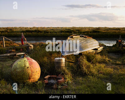 An upturned fishing boat by a narrow water channel in a flat landscape. Fishing floats and buoys.
