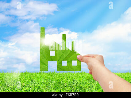 Hand hold factory icon on field and blue sky background, Eco green factory concept Stock Photo