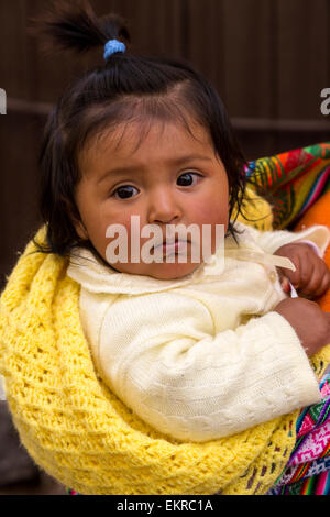 Peru, Cusco.  Young Quechua Girl being Carried on her Mother's  Back. Stock Photo