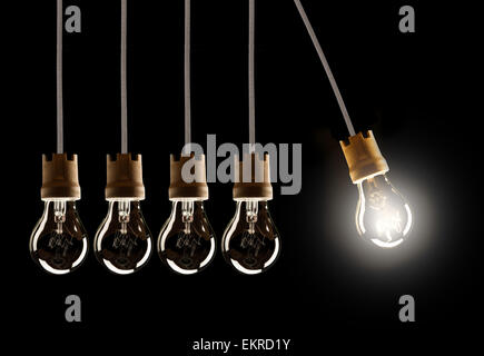 Light bulbs in row with single one in motion and shinning, isolated on black background Stock Photo
