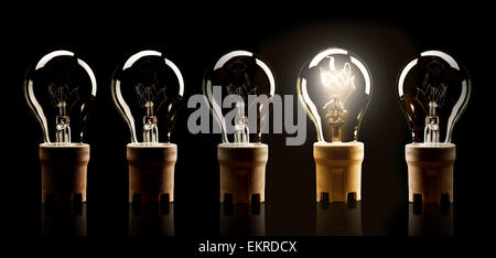 Light bulbs in row with single one shinning, isolated on black background Stock Photo