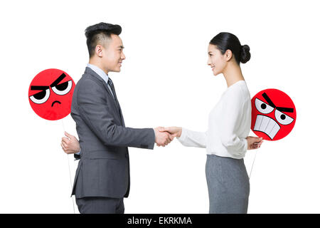 Business person shaking hands with angry emoticon faces behind their backs Stock Photo