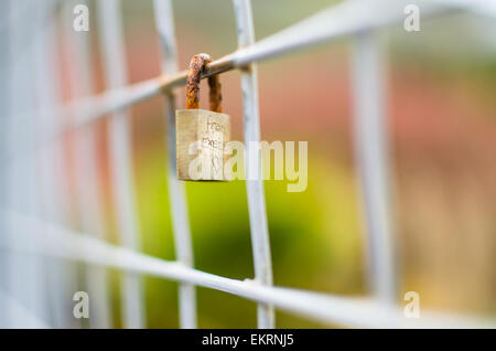 A closed metal padlock is locked onto a section of square fence. Etched onto the padlock is 'from Exeter' with shallow focus. Stock Photo