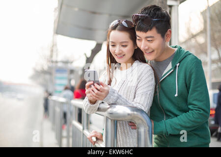 Young couple using smart phone at bus stop Stock Photo