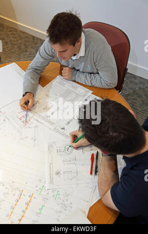 Two young engineers discuss and amend construction drawings whilst seated at a meeting room table. High level view. Stock Photo
