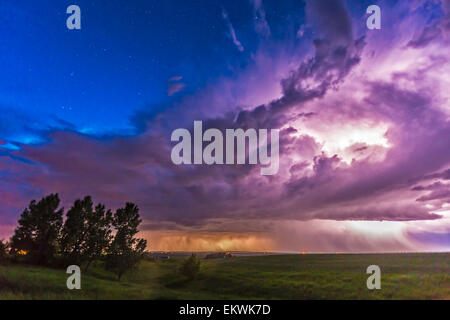 June 20, 2014 - A massive thunderstorm moves across the northern horizon lit internally by lightning. The clear sky behind it is Stock Photo