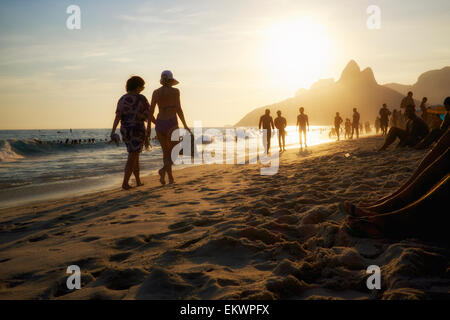 Silhouettes of Brazilian women walking in bikinis along the shore in bright sunset at Posto Nove Ipanema Beach Rio de Janeiro Stock Photo