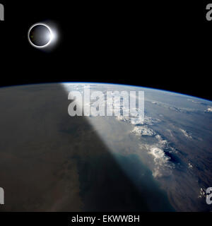 A solar eclipses partially shades the Earth below while the emerging sun lights the remainder of the planet. Stock Photo